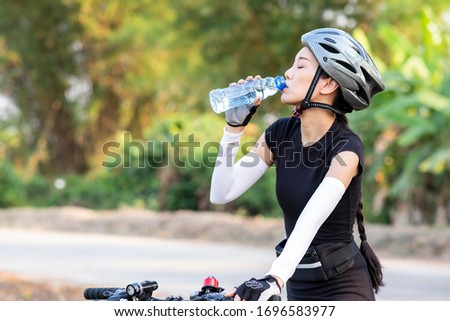 Sporty woman riding a mountain bike in the natural background and drinking bottled water