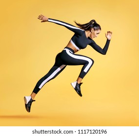 Спортивная женщина бегун в силуэт на желтом фоне. Фото привлекательной женщины в модной спортивной одежде. Динамическое движение. Вид сбоку. Спорт и здоровый образ жизни