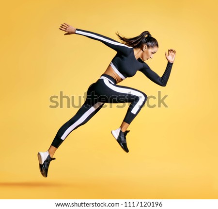 Sporty woman runner in silhouette on yellow background. Photo of attractive woman in fashionable sportswear. Dynamic movement. Side view. Sport and healthy lifestyle
