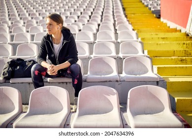Sporty woman sitting alone on the bleachers at the daylight