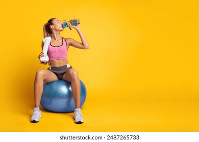 Sporty Woman Sitting On Fitball Drinking Water Over Pink Background In Studio. Workout Break Concept. Empty Space - Powered by Shutterstock