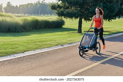 Sporty woman in sportswear running with baby stroller at sunny morning in city park during motherhood time for recovery health