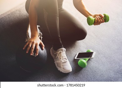 Sporty woman using smartphone during workout at home in the living room.Online personal trainer or on mobile phone.Sport and recreation concept.