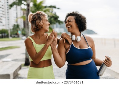 Sporty women high fiving each other in fitness wear, celebrating a successful workout session outdoors. Two fitness friends with different body sizes embrace a healthy lifestyle together. - Powered by Shutterstock