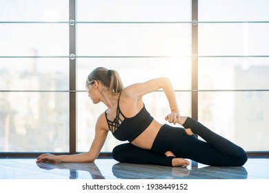 Sporty yoga girl in pigeon pose. Woman in black sportswear doing stretching