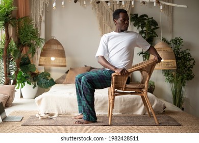 Sporty young african man practicing yoga using chair, doing Revolved Chair Pose, Parivrtta Utkatasana