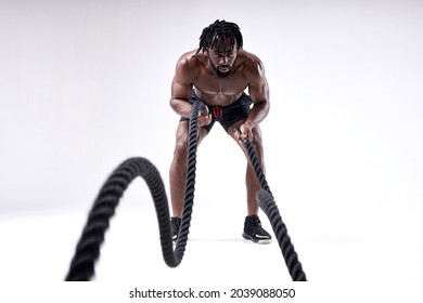 Sporty Young Black Man Doing Cross Fit Exercises With Ropes Over Isolated White Background, Training. Hard Workout. Wave. Shirtless Fit Athlete Guy Is Concentrated On Workout, Sport. Portrait