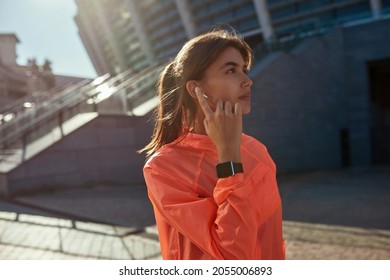 Sporty young Caucasian woman in sportswear listen music in wireless earphones train workout on street. Active fit millennial girl use headphones app run jog follow healthy lifestyle. Sport concept.