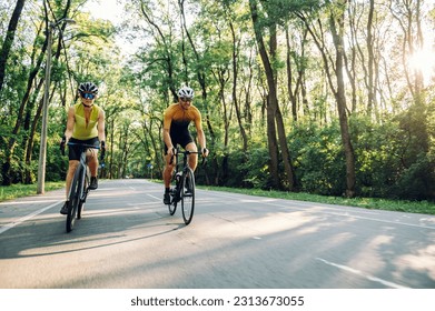 Sporty young couple on bicycles during weekend cycle ride outside of the city. Wearing sports clothes and helmets. Traveling by high-performance sport bicycles. Sports lifestyle. Copy space.
