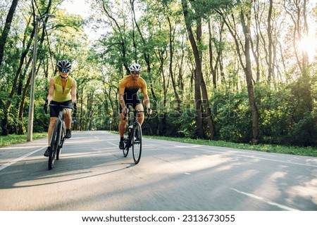 Sporty young couple on bicycles during weekend cycle ride outside of the city. Wearing sports clothes and helmets. Traveling by high-performance sport bicycles. Sports lifestyle. Copy space.