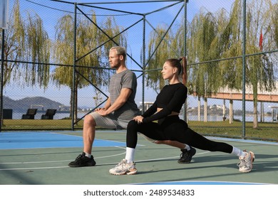 Sporty young couple working out on a basketball court outdoors. Couple goals concept. Boyfriend and girlfriend stretching in the park, doing lunges. Copy space, background. - Powered by Shutterstock