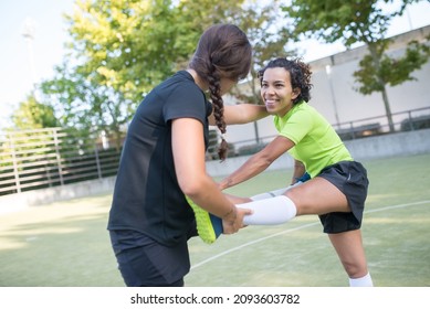 Sporty young female friends warming up on football field. Sportswomen in colorful uniforms helping each other to stretch. Sport, leisure, active lifestyle concept - Powered by Shutterstock