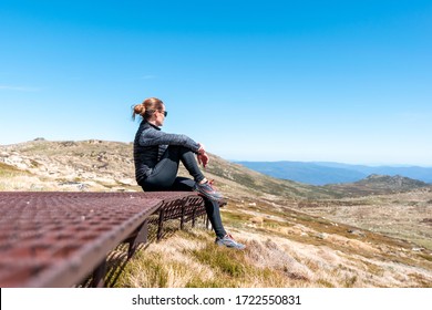 Sporty young female hiker taking a break sitting on the rusty steel boardwalk near the summit of Mount Kosciuszko (2228m above sea level) Kosciuszko National Park, New South Wales, Australia.
