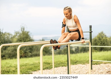 Sporty young female working out calisthenics in an outdoor gym using parallel bars. Beautiful blonde girl with braids works out outdoors doing push-ups on an elevated bar.  - Powered by Shutterstock