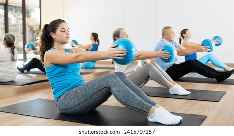 Sporty young girl doing sit-ups with bender ball to strengthen abs muscles during group pilates class in fitness studio - Powered by Shutterstock