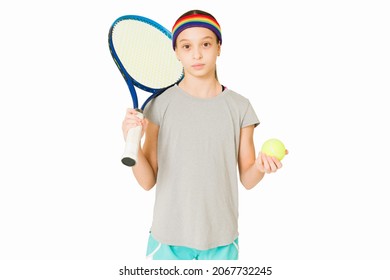 Sporty Young Girl Wearing A Sweat Band And Holding A Tennis Ball With A Racket In Front Of A White Background