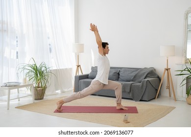 Sporty Young Man is Making Lunge Warrior Yoga Pose in Living Room at Home. Male is Stretching Him Legs. Boy is Making Physical Exercises. Home Fitness, Yoga Practice, Workout And Wellness Concept - Powered by Shutterstock