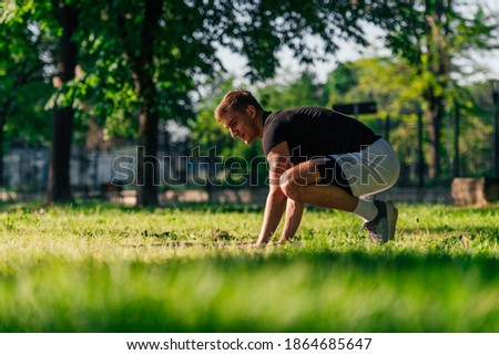 Sporty young man practicing crow pose or bakasana, yoga asana, outdoors in a park