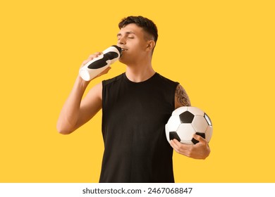 Sporty young man with soccer ball drinking water on yellow background - Powered by Shutterstock