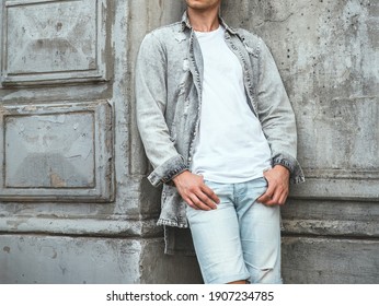 A Sporty Young Man Stands Against An Old Concrete Wall. The Guy Is Wearing A White T-shirt, Shirt And Jeans.