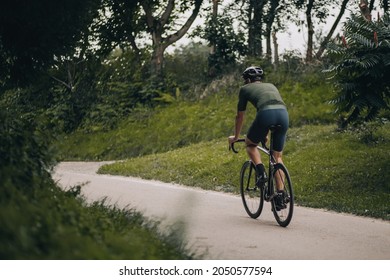 Sporty Young Man Wearing Protective Helmet Riding Black Bike At Green City Park. Active Man Enjoying Favorite Hobby On Fresh Air. Concept Of Healthy Lifestyles.