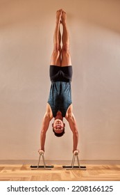Sporty young man working out, yoga, pilates, fitness training, doing handstand, Adho Mukha Vrksasana, Downward facing Tree Pose, back view, low key shot.