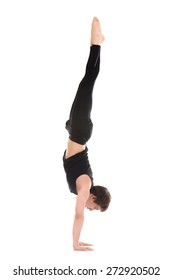 Sporty young man working out, yoga, pilates, fitness training, doing handstand, Adho Mukha Vrksasana, Downward facing Tree Pose, side view
