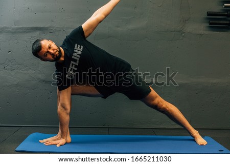 Sporty young man working out, doing handstand yoga. Studio shot in urban fitness gym with grey background for copy space.