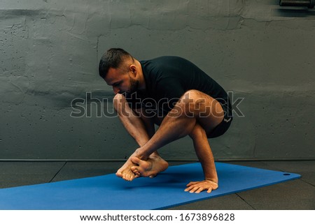 Sporty young man working out, doing handstand yoga. Studio shot in urban fitness gym with grey background for copy space.