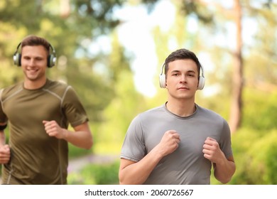 Sporty young men with headphones running in park - Shutterstock ID 2060726567