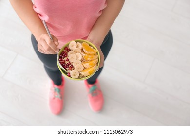 Sporty young woman with bowl of tasty oatmeal indoors