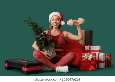 Sporty young woman with dumbbell, Christmas tree, gift boxes and aerobic stepper on green background - Powered by Shutterstock