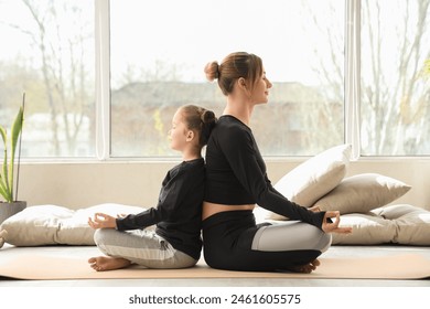 Sporty young woman with her little daughter meditating on yoga mat at home - Powered by Shutterstock