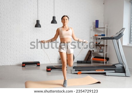 Sporty young woman with jumping rope training in gym