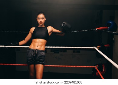 Sporty young woman looking at the camera while standing against the ropes in a boxing ring. Female boxer training in a fitness gym. - Powered by Shutterstock