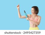 Sporty young woman massaging her arm with roller on blue background