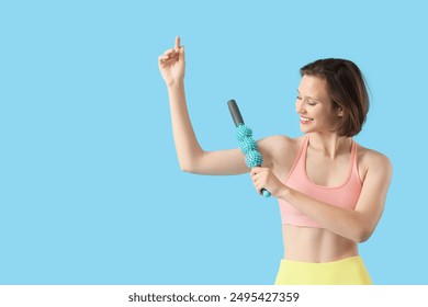 Sporty young woman massaging her arm with roller on blue background