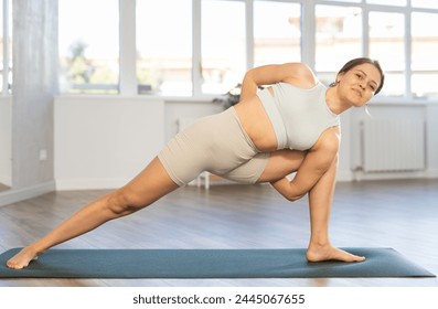 Sporty young woman performing Baddha Parsvakonasana, Bound Side Angle Pose, during daily yoga practice in sunny cozy studio.... - Powered by Shutterstock