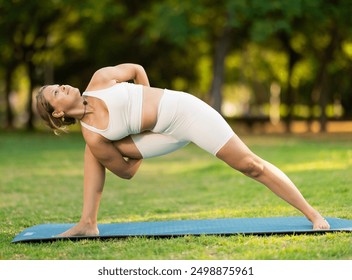 Sporty young woman performing Baddha Parsvakonasana, Bound Side Angle Pose, during yoga practice outdoors on green meadow in city park on sunny summer day.. - Powered by Shutterstock