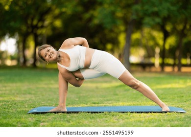 Sporty young woman performing Baddha Parsvakonasana, Bound Side Angle Pose, during yoga practice outdoors on green meadow in city park on sunny summer day.. - Powered by Shutterstock