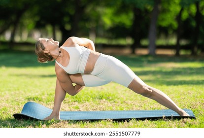 Sporty young woman performing Baddha Parsvakonasana, Bound Side Angle Pose, during yoga practice outdoors on green meadow in city park on sunny summer day.. - Powered by Shutterstock