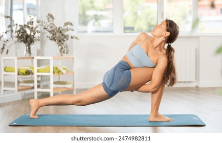 Sporty young woman performing stretching asana Baddha Parsvakonasana, or Bound Side Angle Pose, during daily yoga practice in sunny cozy studio.. - Powered by Shutterstock