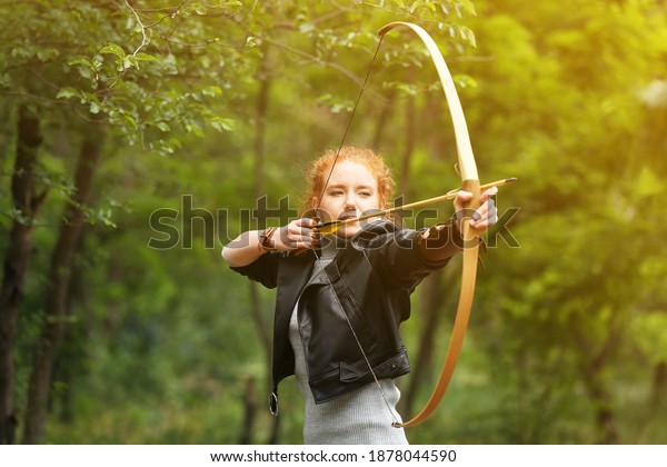 Sporty young\
woman practicing archery\
outdoors