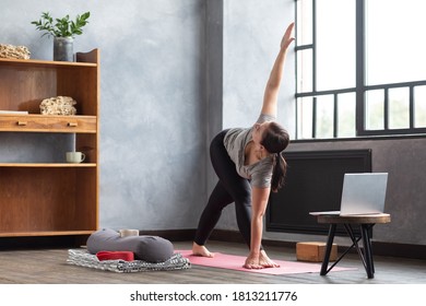 Sporty young woman practicing yoga, doing Revolved Triangle Pose, Parivrrta Trikonasana, working out at home