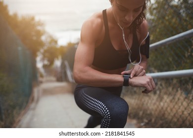 Sporty young woman setting up her smartphone while climbing a staircase outdoors. Athletic young woman going out for a morning run. - Powered by Shutterstock