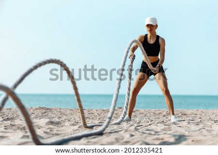 Sporty young woman training with a battle rope, Man doing fitness workout on the beach on a sunny day using two battle ropes on the beach