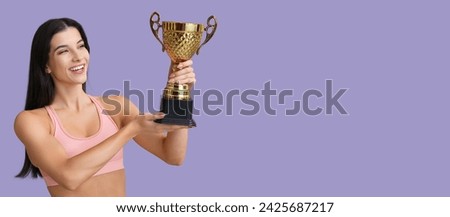 Sporty young woman with trophy cup on lilac background with space for text
