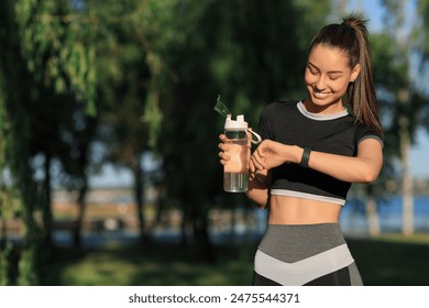 Sporty young woman with water bottle and fitness tracker in park - Powered by Shutterstock