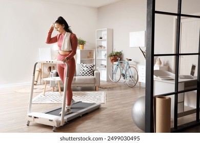 Sporty young woman wiping sweat on treadmill at home