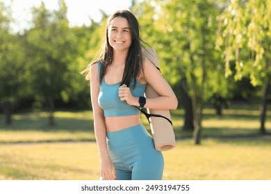 Sporty young woman with yoga mat and fitness tracker in park - Powered by Shutterstock